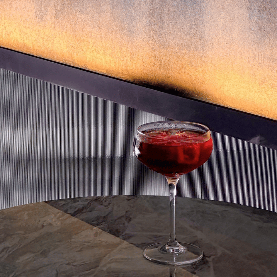 ADDICT 沉癮餐酒館創意特色調酒,深紅色酒液盛裝於高腳杯,背景為極簡金屬質感牆面,展現東區餐酒館深夜飲酒風格