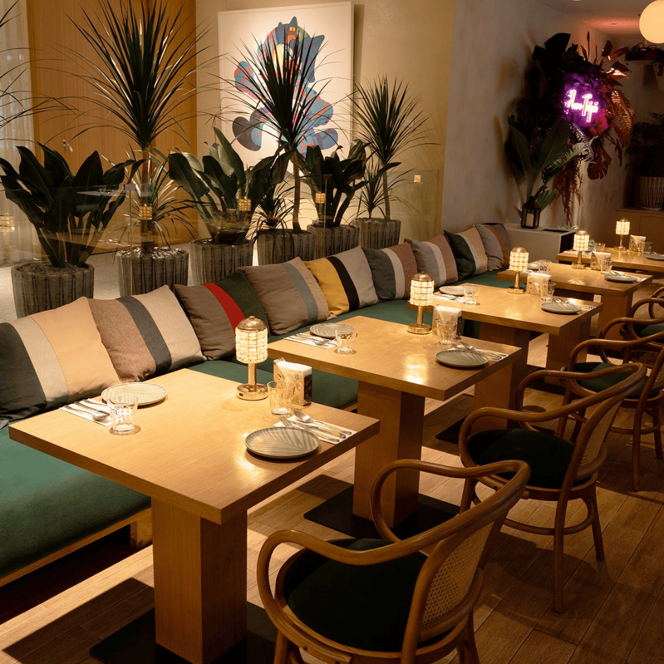 Flare Taipei 室內用餐區環境,質感木質餐桌搭配綠色長沙發、霓虹裝飾與熱帶盆栽,適合情侶約會或多人聚餐的信義區餐酒館