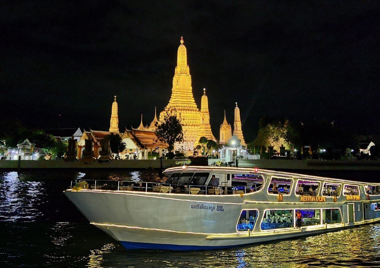 ICONSIAM 昭披耶河晚餐巡遊郵輪行駛於夜間河上，背景為燈光璀璨的鄭王廟（黎明寺）
