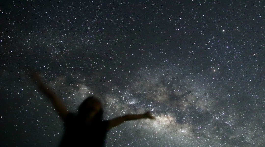 石垣島夜晚星空與璀璨銀河景觀，旅人在星空下張開雙手。